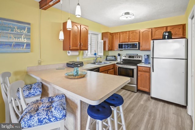 kitchen featuring appliances with stainless steel finishes, kitchen peninsula, sink, and hanging light fixtures