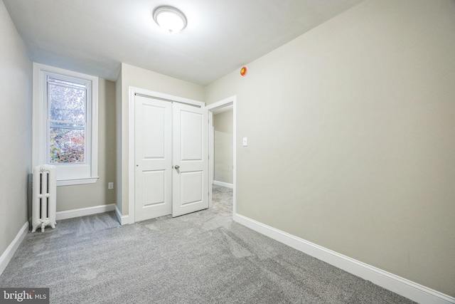 unfurnished bedroom featuring radiator, a closet, and light colored carpet