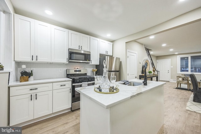 kitchen featuring stainless steel appliances, sink, white cabinets, light hardwood / wood-style floors, and an island with sink