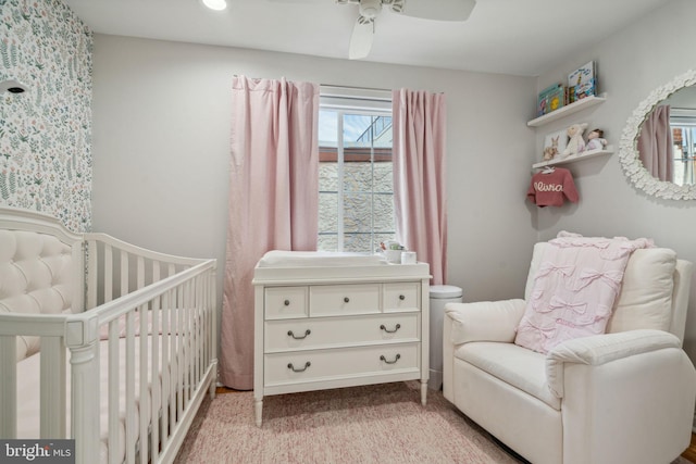 carpeted bedroom featuring a crib and ceiling fan