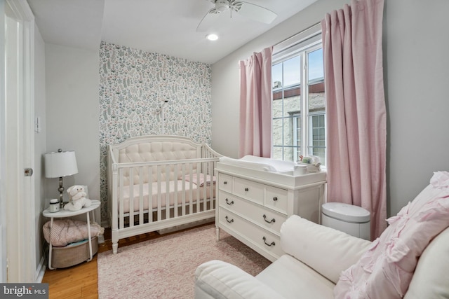 bedroom featuring a crib, light hardwood / wood-style floors, and ceiling fan