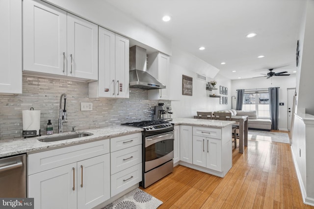 kitchen featuring white cabinets, sink, wall chimney exhaust hood, light wood-type flooring, and stainless steel appliances