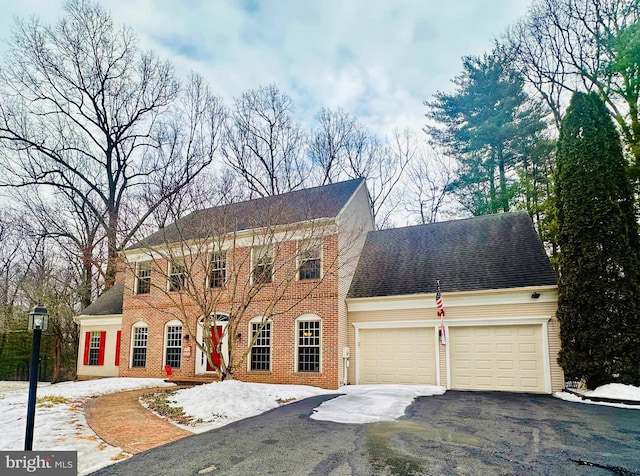 colonial house featuring a garage, roof with shingles, aphalt driveway, and brick siding