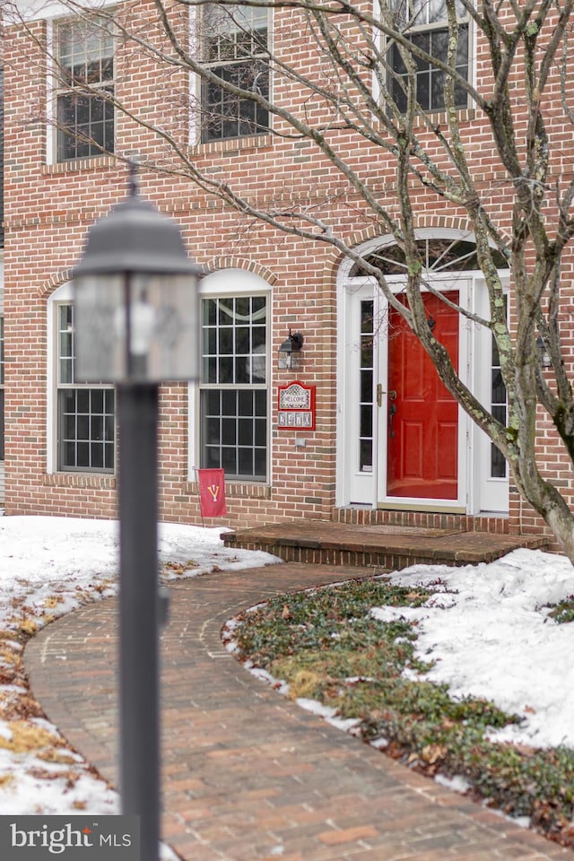 snow covered property entrance featuring brick siding