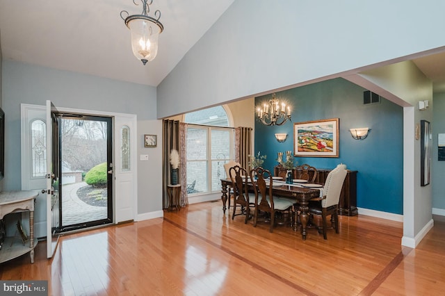 dining area featuring a notable chandelier, wood-type flooring, and high vaulted ceiling