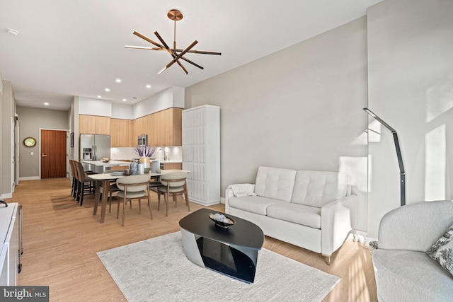 living room with a notable chandelier, sink, a high ceiling, and light hardwood / wood-style flooring