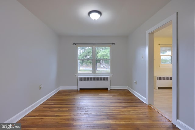 unfurnished room featuring dark hardwood / wood-style flooring, radiator, and a healthy amount of sunlight