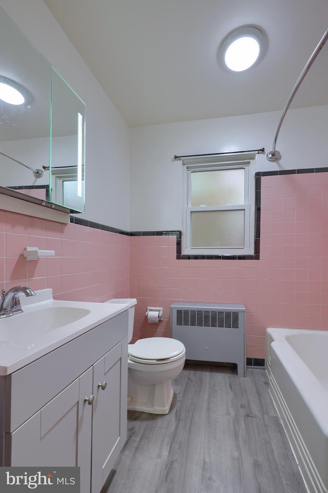 full bathroom with hardwood / wood-style floors, radiator heating unit, and tile walls