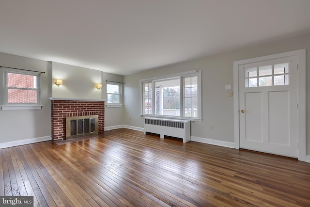 unfurnished living room with radiator heating unit, dark hardwood / wood-style floors, and a brick fireplace