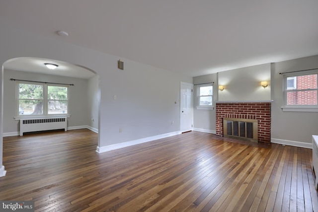 unfurnished living room featuring radiator, dark hardwood / wood-style flooring, and a healthy amount of sunlight