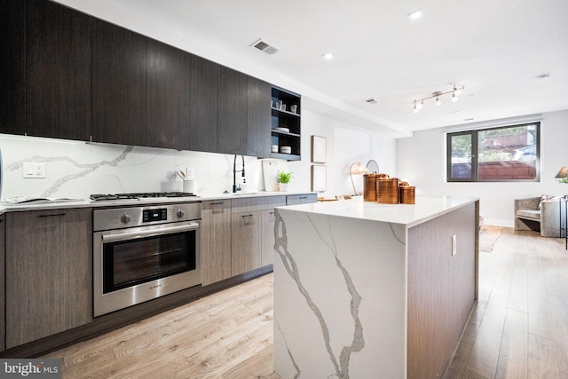 kitchen with sink, decorative backsplash, light wood-type flooring, a kitchen island, and stainless steel appliances