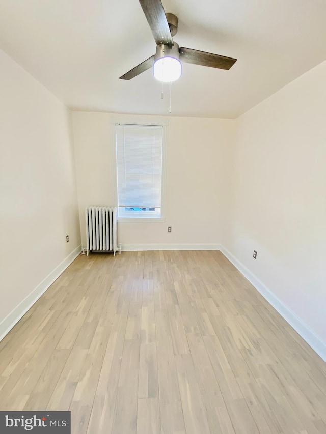 spare room featuring ceiling fan, radiator heating unit, and light hardwood / wood-style flooring