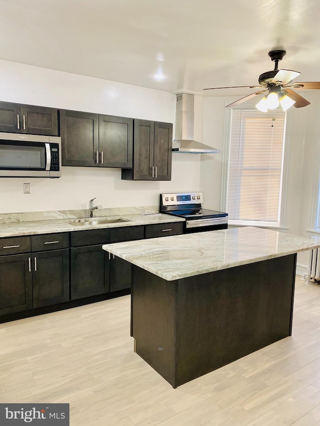 kitchen with sink, light hardwood / wood-style flooring, wall chimney range hood, and appliances with stainless steel finishes