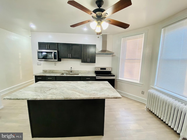 kitchen with radiator, a center island, sink, stainless steel appliances, and wall chimney range hood