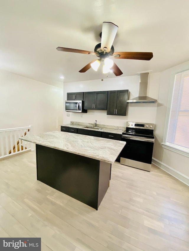 kitchen with light stone countertops, wall chimney range hood, appliances with stainless steel finishes, and light hardwood / wood-style flooring