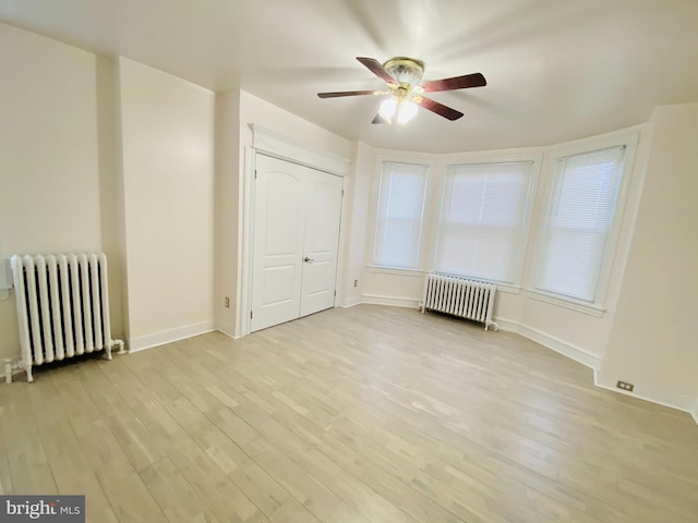 unfurnished bedroom featuring a closet, ceiling fan, radiator heating unit, and light wood-type flooring