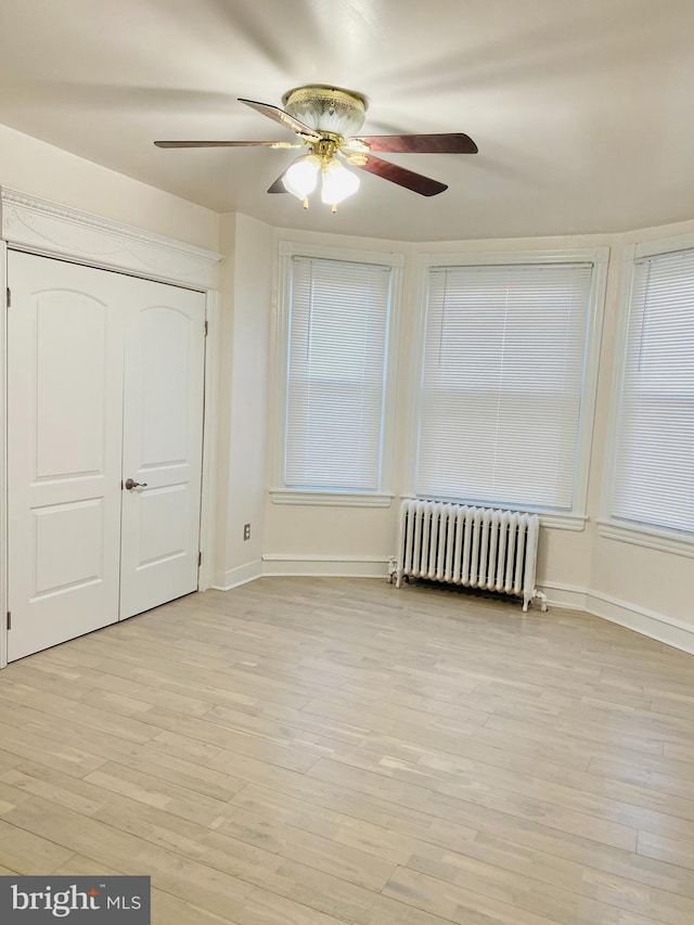 unfurnished bedroom featuring ceiling fan, a closet, radiator heating unit, and light hardwood / wood-style flooring