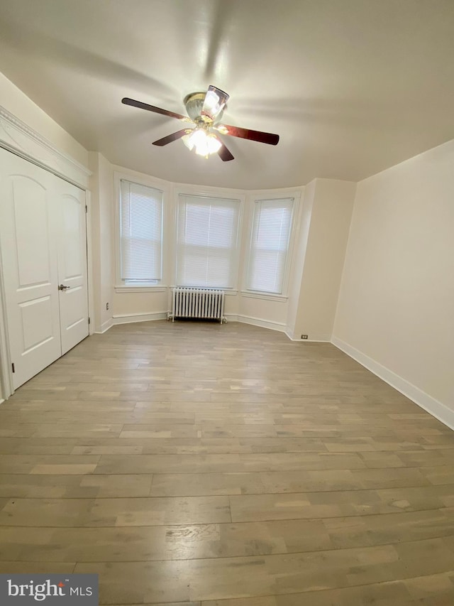 bonus room featuring ceiling fan, radiator heating unit, and light wood-type flooring