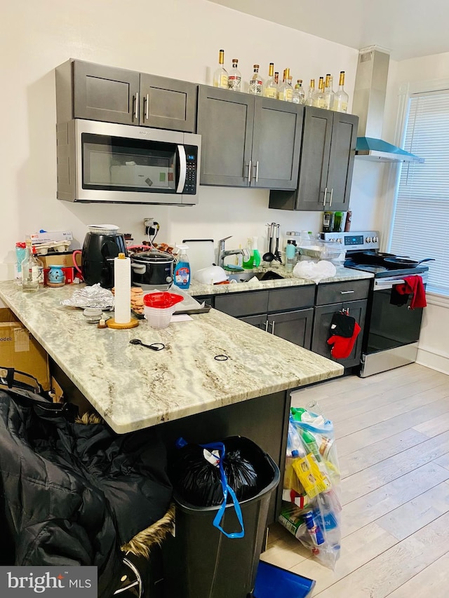 kitchen featuring sink, light stone counters, extractor fan, appliances with stainless steel finishes, and light wood-type flooring