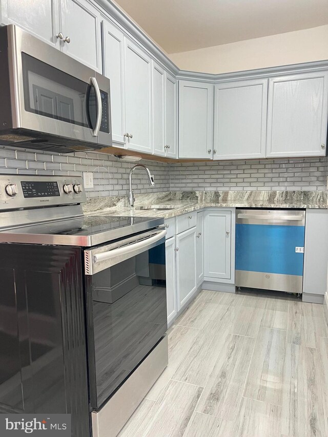 kitchen featuring appliances with stainless steel finishes, light wood-type flooring, tasteful backsplash, and sink