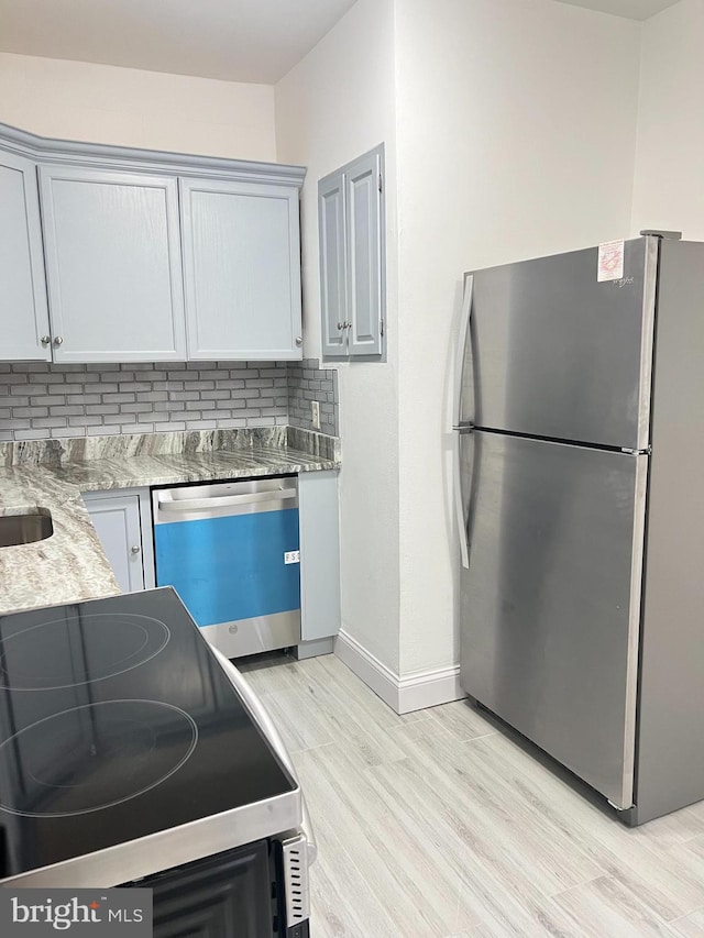 kitchen with gray cabinetry, light hardwood / wood-style flooring, light stone countertops, tasteful backsplash, and stainless steel appliances