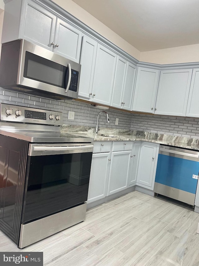 kitchen featuring light stone countertops, appliances with stainless steel finishes, light wood-type flooring, and backsplash