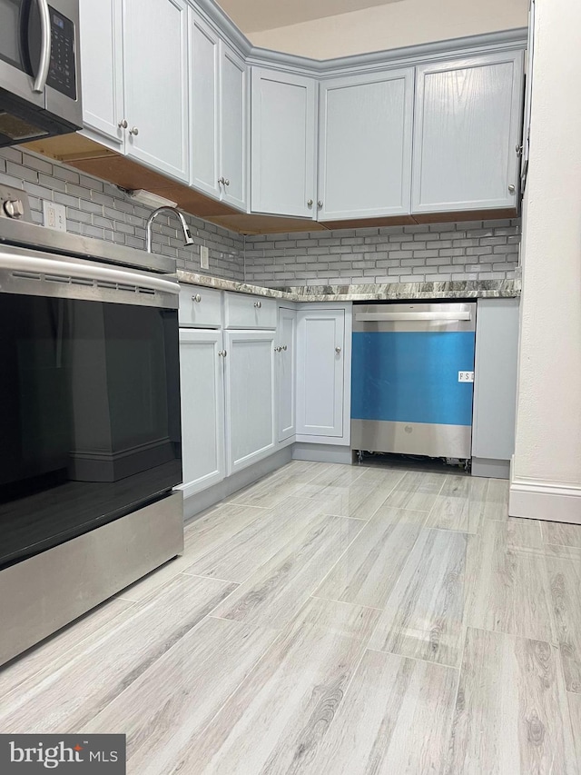 kitchen featuring light hardwood / wood-style floors, light stone countertops, stainless steel appliances, and tasteful backsplash