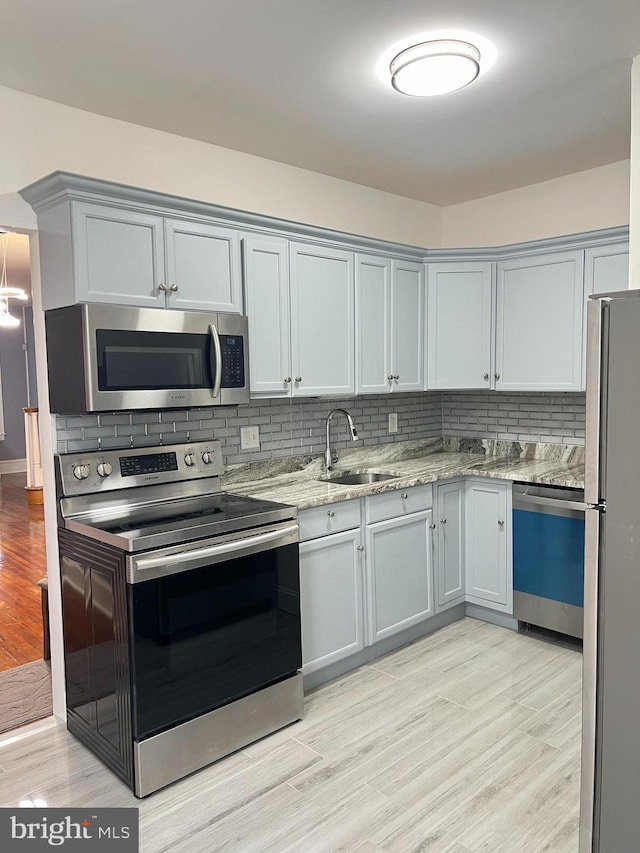 kitchen featuring decorative backsplash, light wood-type flooring, light stone counters, stainless steel appliances, and sink