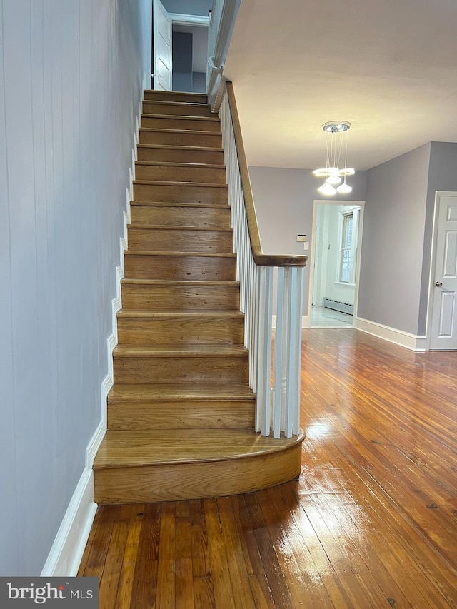 staircase featuring hardwood / wood-style floors, a baseboard radiator, and an inviting chandelier