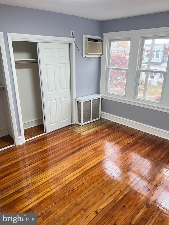 unfurnished bedroom featuring a wall unit AC and hardwood / wood-style flooring