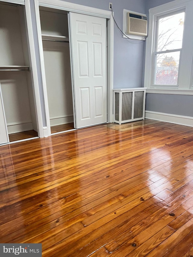 unfurnished bedroom with an AC wall unit, multiple closets, and wood-type flooring