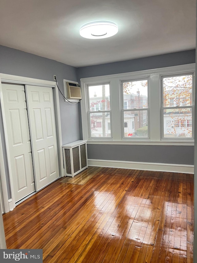 unfurnished bedroom with dark hardwood / wood-style floors, a wall mounted AC, and a closet