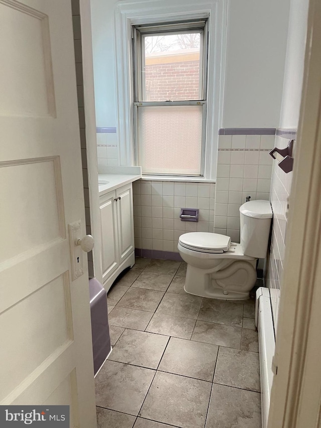 bathroom with baseboard heating, tile patterned flooring, toilet, vanity, and tile walls