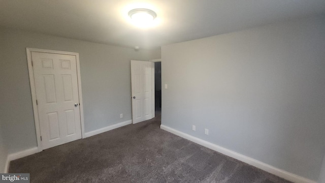 unfurnished bedroom with dark carpet and baseboards