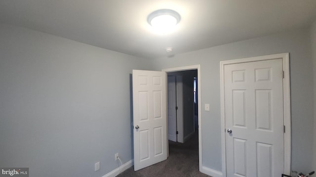 unfurnished bedroom with dark colored carpet and baseboards