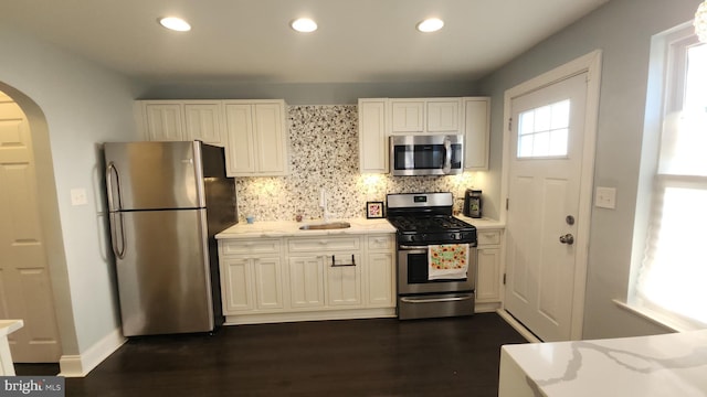 kitchen with backsplash, arched walkways, stainless steel appliances, and light stone counters