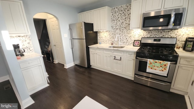 kitchen with white cabinets, appliances with stainless steel finishes, arched walkways, and a sink