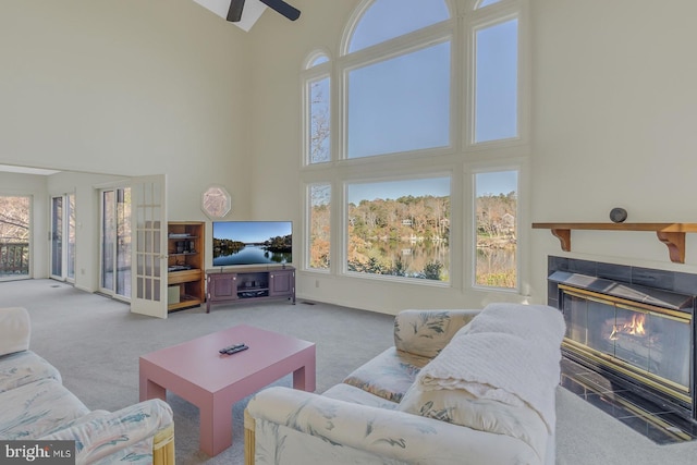 carpeted living room featuring ceiling fan, a healthy amount of sunlight, a towering ceiling, and a fireplace