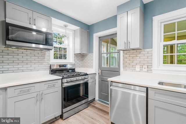 kitchen with appliances with stainless steel finishes, light wood-type flooring, tasteful backsplash, and sink