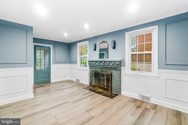 unfurnished living room with a stone fireplace, a wealth of natural light, light hardwood / wood-style flooring, and crown molding