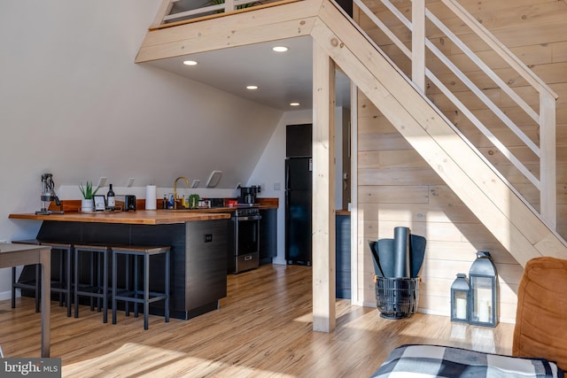 bar with light wood-type flooring, butcher block countertops, black fridge, and vaulted ceiling