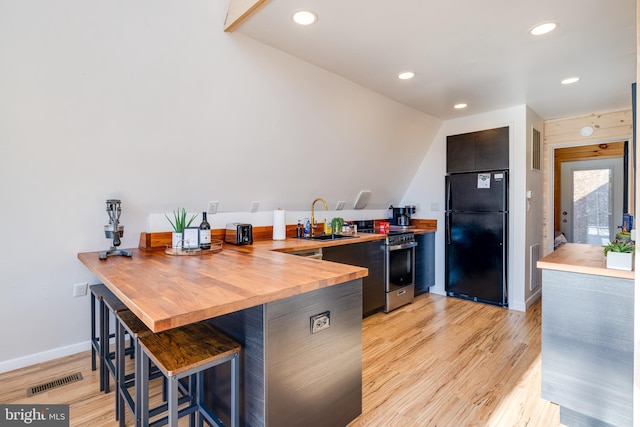 kitchen featuring black fridge, sink, light hardwood / wood-style flooring, stainless steel range, and a breakfast bar area