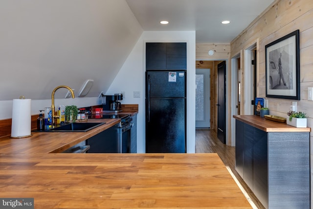 kitchen with black refrigerator, sink, wooden walls, dark hardwood / wood-style floors, and butcher block counters