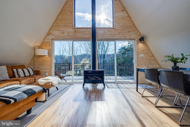 sitting room with plenty of natural light, wood walls, light wood-type flooring, and high vaulted ceiling