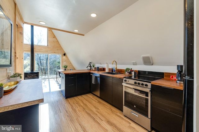 kitchen featuring sink, stainless steel appliances, wood counters, wooden walls, and light wood-type flooring