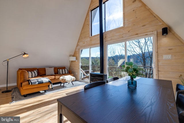 dining room with hardwood / wood-style flooring, high vaulted ceiling, wood walls, and a wealth of natural light