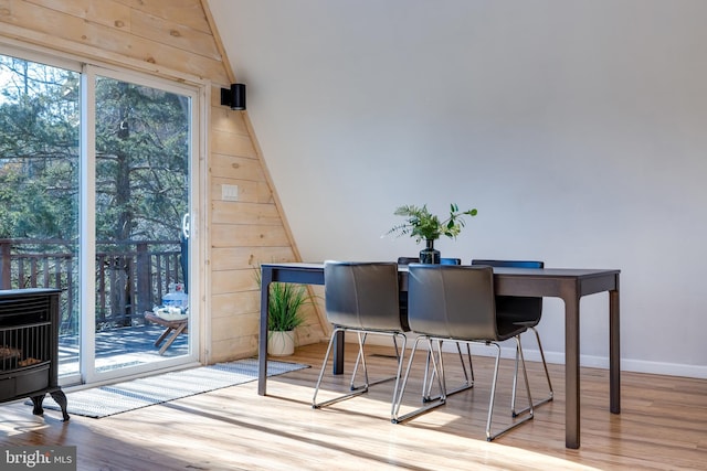 dining area with light wood-type flooring, a wood stove, and wooden walls