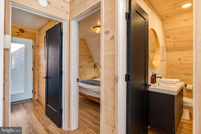 corridor with wooden walls, sink, and light hardwood / wood-style floors