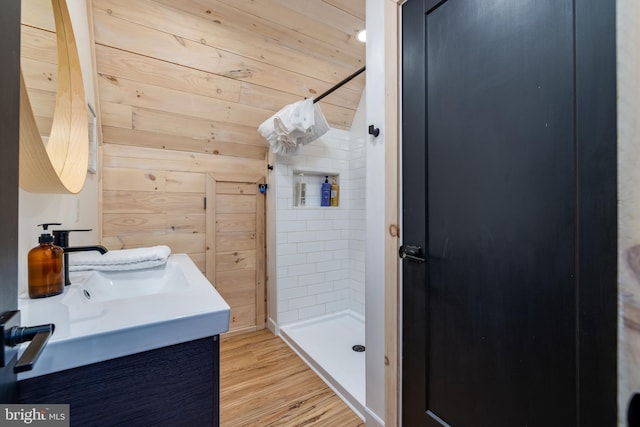 bathroom with hardwood / wood-style flooring, vanity, wood walls, and tiled shower