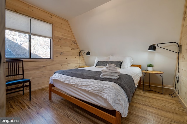 bedroom featuring lofted ceiling, hardwood / wood-style flooring, and wooden walls